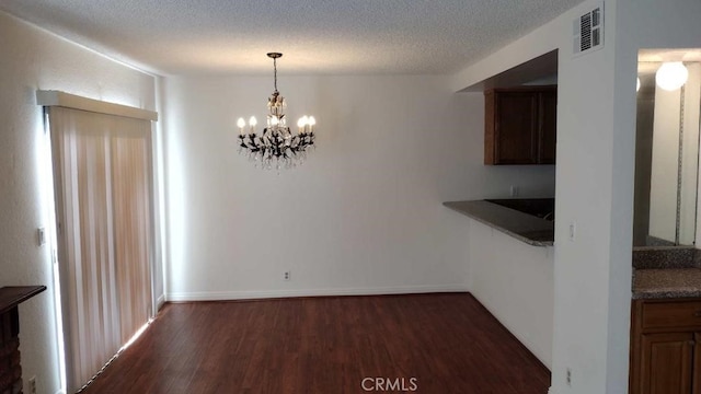 unfurnished dining area featuring a textured ceiling, dark wood-type flooring, and an inviting chandelier