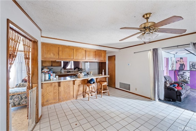 kitchen with a textured ceiling, kitchen peninsula, ceiling fan, ornamental molding, and white refrigerator