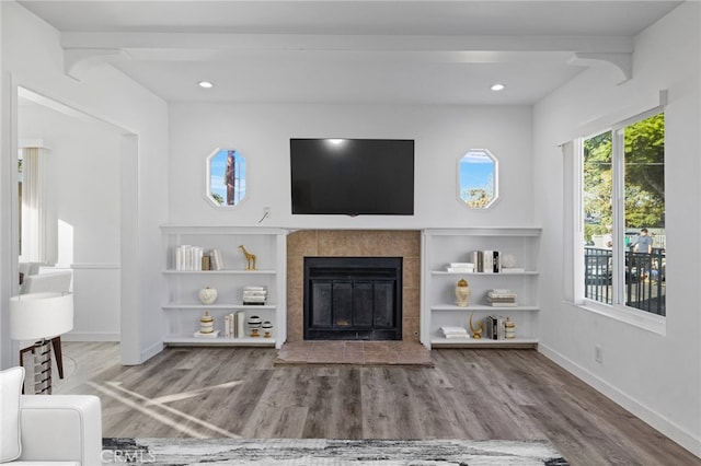 unfurnished living room with a tiled fireplace, hardwood / wood-style flooring, and beam ceiling