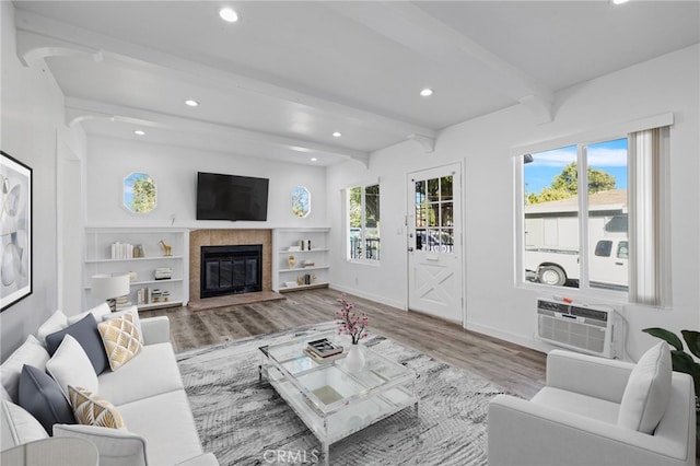 living room featuring a wall mounted AC, beamed ceiling, wood-type flooring, and plenty of natural light