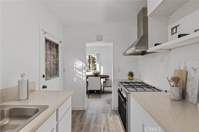 kitchen with high end range, white cabinets, wall chimney range hood, and light hardwood / wood-style flooring