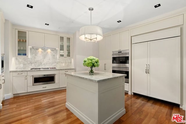 kitchen featuring hardwood / wood-style floors, light stone counters, appliances with stainless steel finishes, decorative light fixtures, and a center island