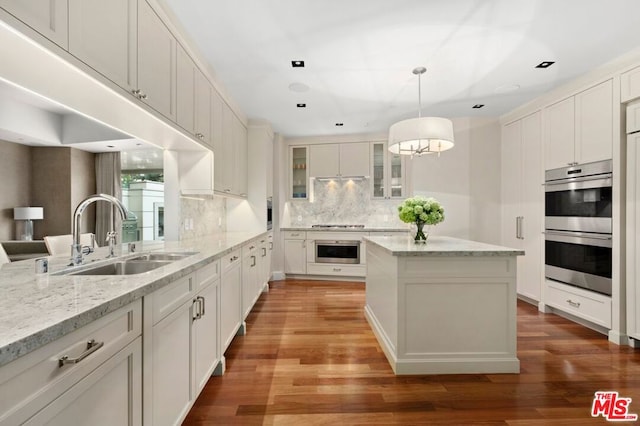 kitchen with stainless steel double oven, hardwood / wood-style flooring, sink, light stone countertops, and pendant lighting