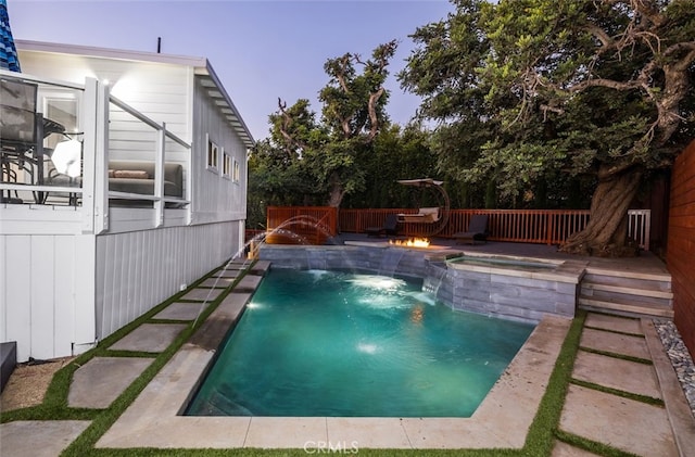 pool at dusk with pool water feature and an in ground hot tub