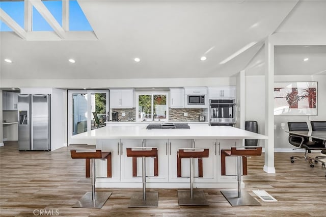 kitchen featuring white cabinetry, appliances with stainless steel finishes, backsplash, and a kitchen bar