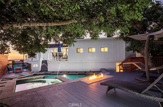 pool at dusk featuring a wooden deck, pool water feature, and a fire pit