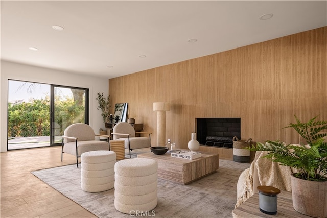 living room with light hardwood / wood-style floors, a large fireplace, and wooden walls