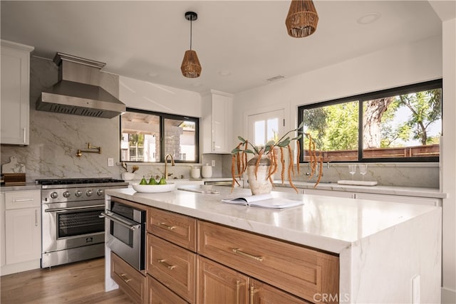 kitchen with wall chimney range hood, white cabinets, and appliances with stainless steel finishes