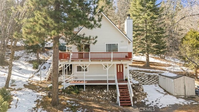 snow covered back of property featuring a wooden deck and a storage shed