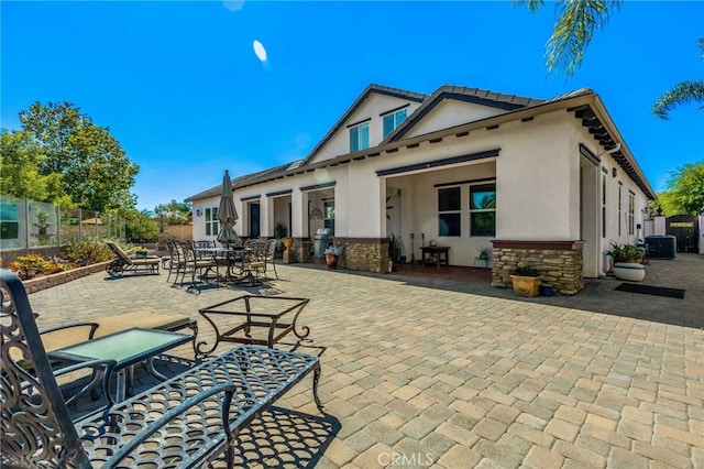 rear view of property featuring stucco siding, stone siding, fence, and a patio area