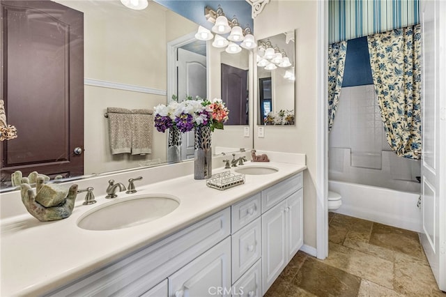 bathroom with double vanity, stone finish floor, toilet, and a sink