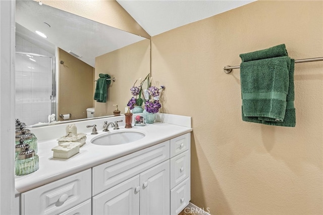 bathroom featuring visible vents, toilet, tiled shower, vanity, and vaulted ceiling