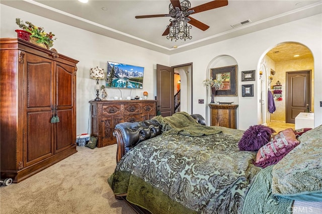 bedroom featuring a ceiling fan, visible vents, a tray ceiling, arched walkways, and light carpet