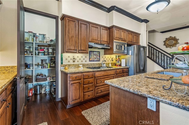 kitchen with light stone counters, dark wood-style flooring, a sink, stainless steel appliances, and under cabinet range hood