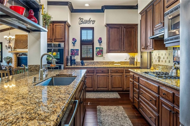 kitchen with a sink, dark wood finished floors, stainless steel appliances, crown molding, and light stone countertops