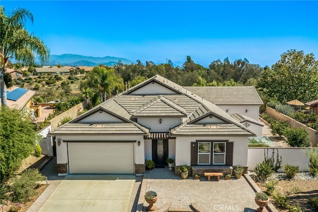 view of front of house with stucco siding, driveway, fence, a mountain view, and an attached garage