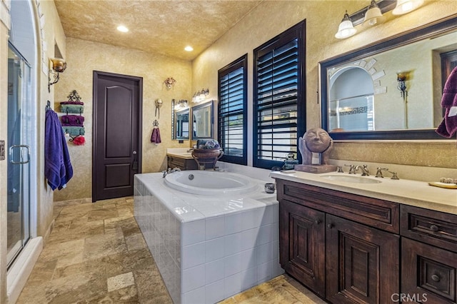 bathroom featuring a shower stall, a garden tub, two vanities, stone tile flooring, and a sink