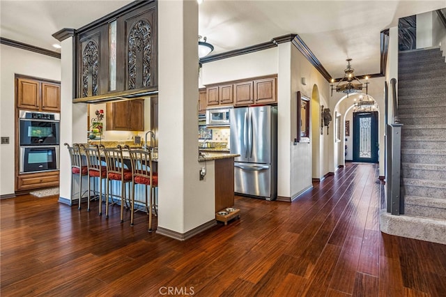 kitchen with dark wood-style floors, stainless steel appliances, arched walkways, crown molding, and light stone countertops