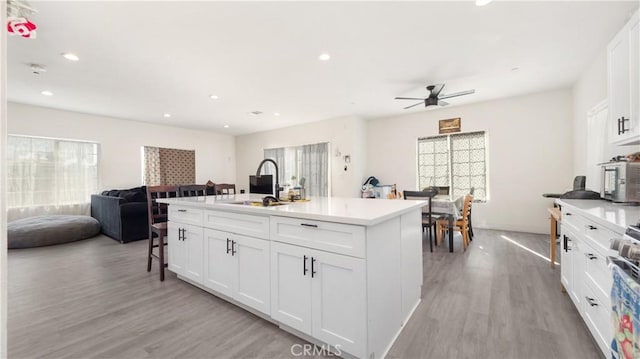 kitchen featuring ceiling fan, a kitchen island with sink, white cabinets, light hardwood / wood-style flooring, and sink