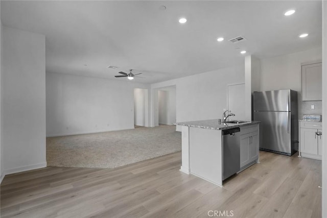 kitchen featuring stainless steel appliances, ceiling fan, sink, light hardwood / wood-style flooring, and an island with sink