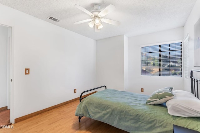 bedroom with ceiling fan, wood-type flooring, and a textured ceiling