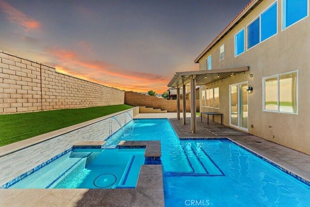 pool at dusk with a patio, pool water feature, and an in ground hot tub