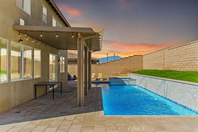 pool at dusk featuring pool water feature and a patio area