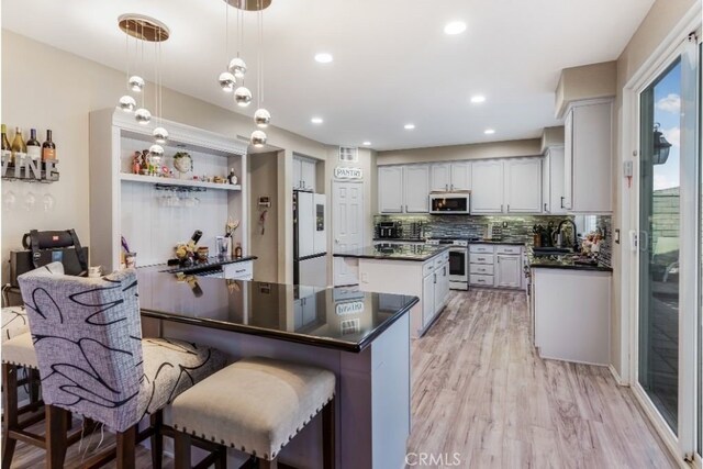 kitchen featuring tasteful backsplash, a kitchen island, appliances with stainless steel finishes, light wood-type flooring, and decorative light fixtures