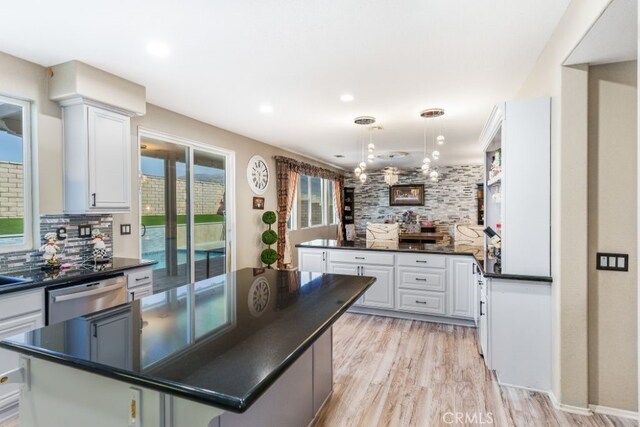 kitchen with a kitchen island, backsplash, pendant lighting, stainless steel dishwasher, and white cabinets