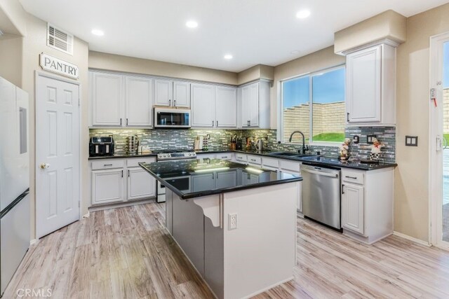 kitchen with sink, a kitchen island, appliances with stainless steel finishes, and light wood-type flooring