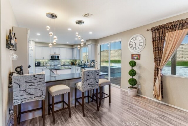 kitchen featuring backsplash, decorative light fixtures, light wood-type flooring, and a wealth of natural light