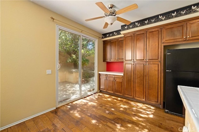 kitchen featuring hardwood / wood-style flooring, ceiling fan, black fridge, and tile countertops