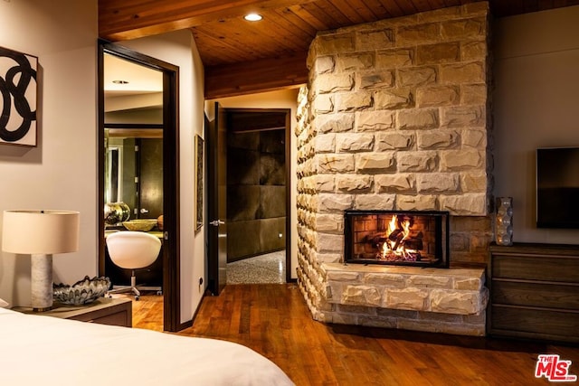 bedroom featuring a stone fireplace, dark hardwood / wood-style floors, and wood ceiling