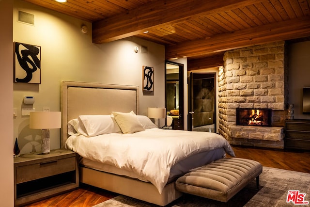 bedroom featuring a stone fireplace, hardwood / wood-style floors, and beam ceiling