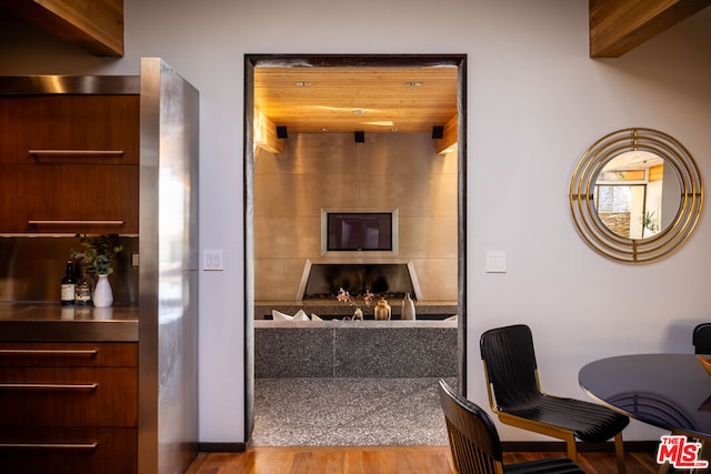 interior space featuring a fireplace, beamed ceiling, stainless steel counters, wood ceiling, and light hardwood / wood-style flooring