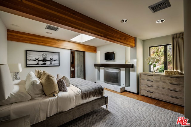 bedroom featuring beam ceiling, a skylight, and light wood-type flooring