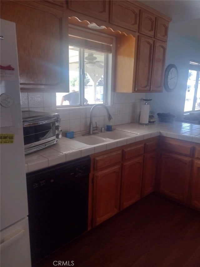 kitchen featuring backsplash, dishwasher, tile counters, sink, and white refrigerator