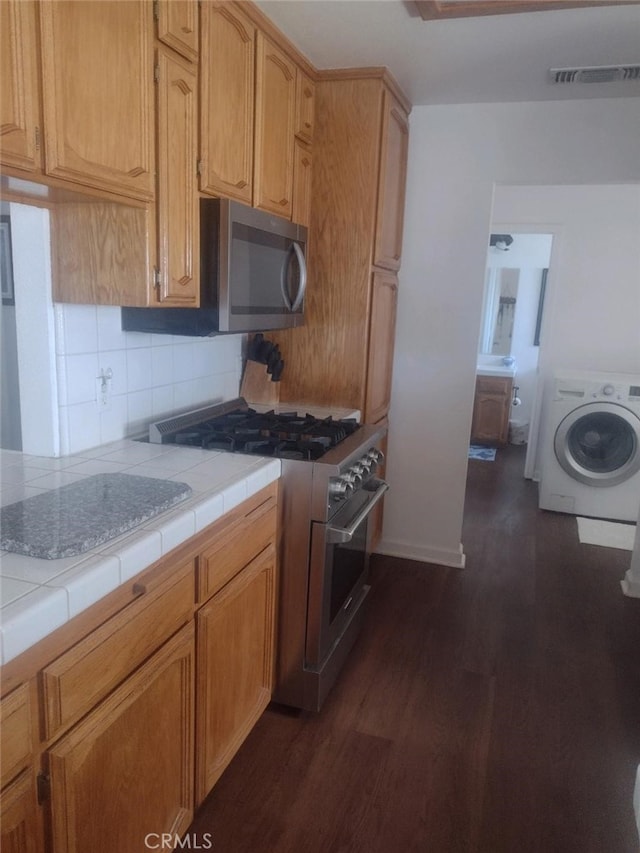 kitchen featuring washer / dryer, backsplash, tile countertops, dark hardwood / wood-style flooring, and stainless steel appliances