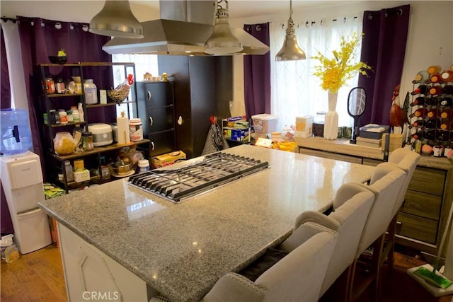 kitchen featuring hanging light fixtures, light stone counters, light hardwood / wood-style flooring, island range hood, and a breakfast bar