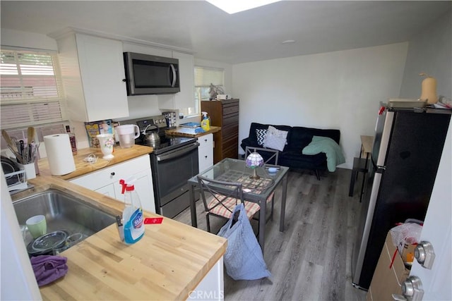 kitchen with sink, stainless steel appliances, butcher block countertops, white cabinets, and light wood-type flooring