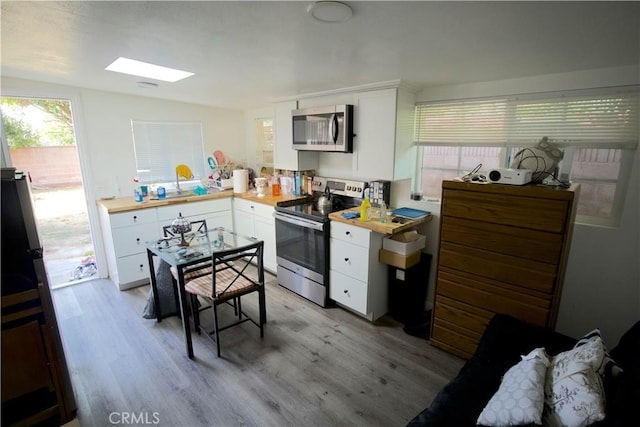 kitchen featuring white cabinets, light hardwood / wood-style floors, vaulted ceiling with skylight, and appliances with stainless steel finishes