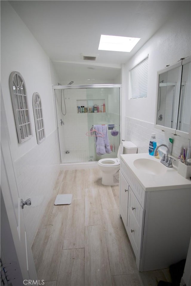 bathroom with a skylight, walk in shower, hardwood / wood-style floors, toilet, and vanity