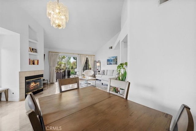 dining room featuring high vaulted ceiling, built in shelves, a tile fireplace, and a chandelier