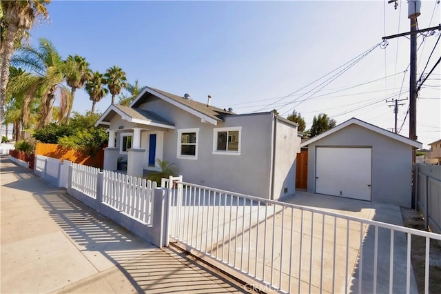 bungalow-style home featuring a fenced front yard, stucco siding, an outdoor structure, and a garage