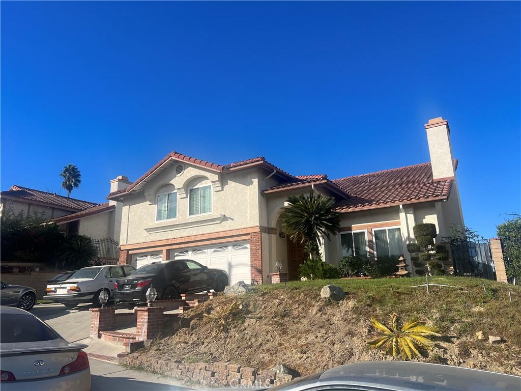 mediterranean / spanish house with stucco siding, a garage, brick siding, a chimney, and a tiled roof