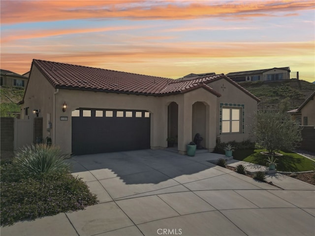 mediterranean / spanish home featuring a tiled roof, concrete driveway, an attached garage, and stucco siding