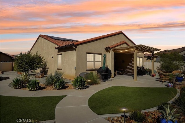 back house at dusk with a lawn, a pergola, and a patio