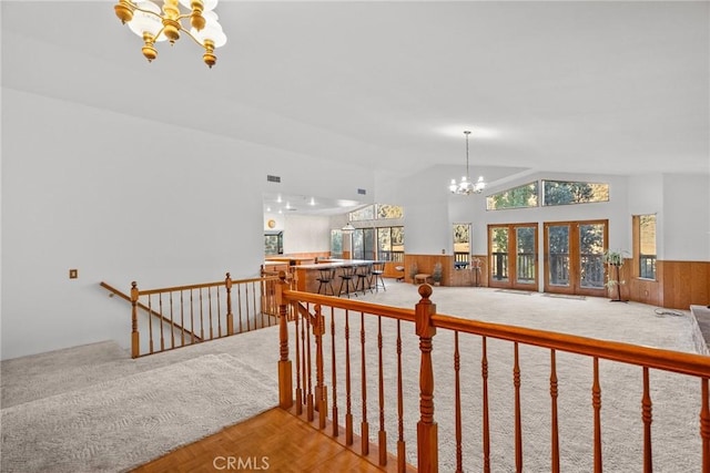 hallway with lofted ceiling, carpet flooring, an inviting chandelier, and wood walls