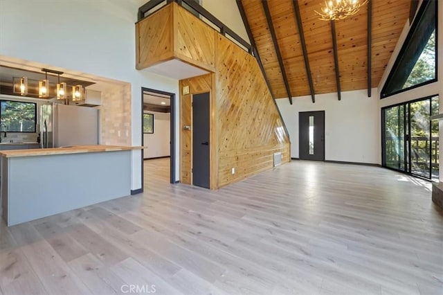 unfurnished living room with beamed ceiling, a wealth of natural light, and light hardwood / wood-style flooring