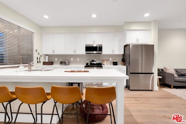 kitchen featuring a kitchen breakfast bar, light wood-type flooring, appliances with stainless steel finishes, tasteful backsplash, and white cabinetry